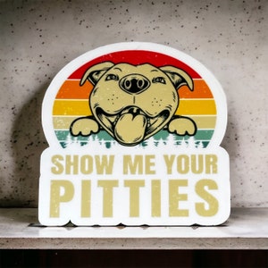 May include: White sticker with a vintage-style sunset background and a cartoon image of a brown and white pit bull dog with its tongue sticking out. The text "Show Me Your Pitties" is printed in yellow on the sticker.