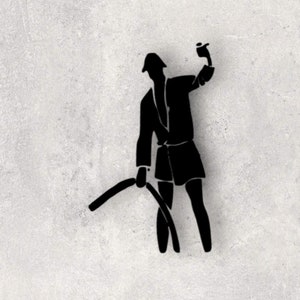 May include: A black silhouette wall decal depicting a figure wearing a hat and jacket, holding a raised object in one hand and a curved, elongated object extending downward in the other hand, creating a distinct graphic shape against the surface.