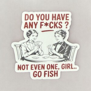 May include: A sticker with a vintage illustration of two women playing cards, with the text "DO YOU HAVE ANY F*CKS?" above them. Below, the text reads "NOT EVEN ONE, GIRL.. GO FISH" in a bold, red font.
