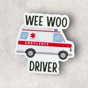 Op de afbeelding: Witte ambulance sticker met rode accenten en de woorden "WEE WOO DRIVER" in zwart. De ambulance heeft een rood kruis en het woord "AMBULANCE" aan de zijkant.