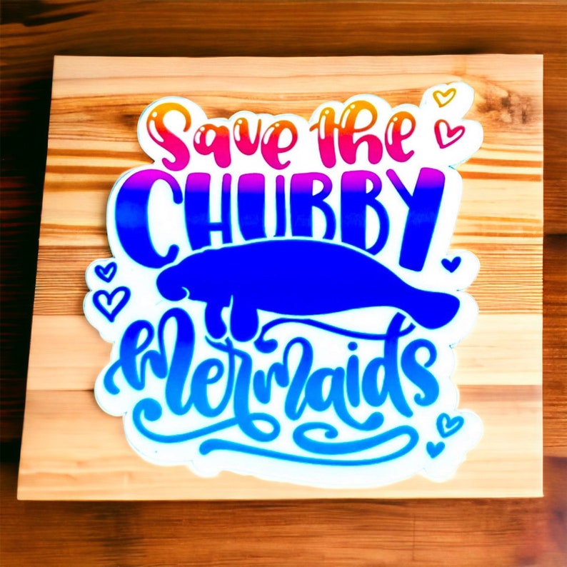 Peut inclure: Une pancarte en bois avec le texte "Save the Chubby Mermaids" en lettres color&eacute;es. Un lamantin bleu est repr&eacute;sent&eacute; en train de nager sous le texte.