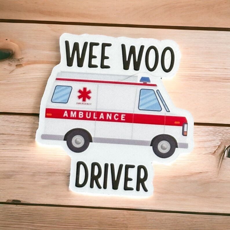 Op de afbeelding: Witte ambulance sticker met een rode streep en de woorden "WEE WOO DRIVER" in het zwart. De ambulance heeft een rood kruis en het woord "AMBULANCE" aan de zijkant.