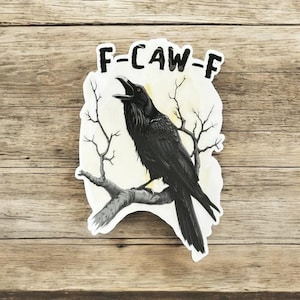 May include: A sticker featuring a black raven perched on a branch, with the text "F-CAW-F" above. The raven is set against a light yellow background with bare tree branches.