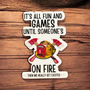 May include: White sticker with black text that reads "It's all fun and games until someone's on fire then we really get excited". A firefighter helmet with crossed axes is in the center of the sticker.