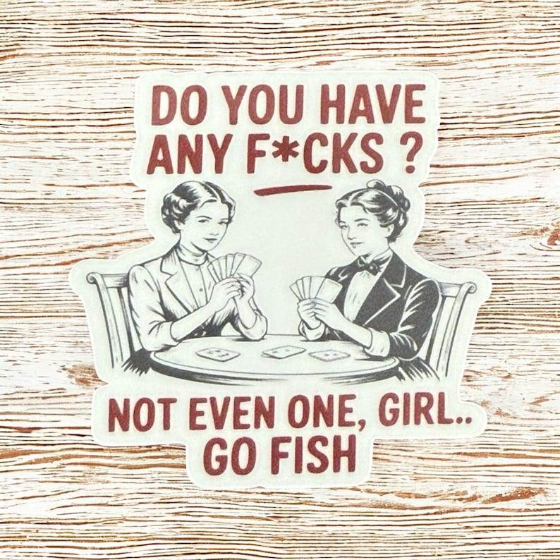May include: A sticker with the text "DO YOU HAVE ANY F*CKS? NOT EVEN ONE, GIRL.. GO FISH." Two women are seated at a table playing cards. The sticker has a white background and a brown border.