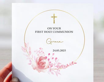 May include: A white card with a gold circle and a cross. The text reads "On your First Holy Communion Grace 24.05.2025". The circle is decorated with pink watercolor flowers.