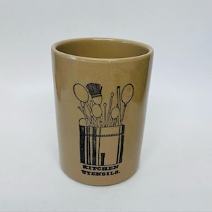 May include: A brown ceramic utensil holder with a black and white illustration of kitchen utensils and the text "KITCHEN UTENSILS."