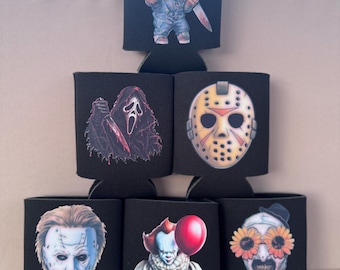 May include: A set of six black foam can coolers arranged in a pyramid. Each cooler features a different horror movie character graphic, including Chucky, Ghostface, Jason Voorhees, Michael Myers, Pennywise with a red balloon, and Art the Clown.