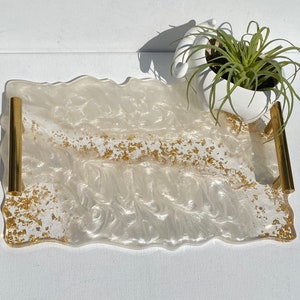 May include: White serving tray with gold flecks and two gold handles. The tray has a wavy edge and a white, marbled appearance.