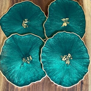 May include: Four green and gold resin coasters with a wavy edge. The coasters have a glittery finish and gold flecks.
