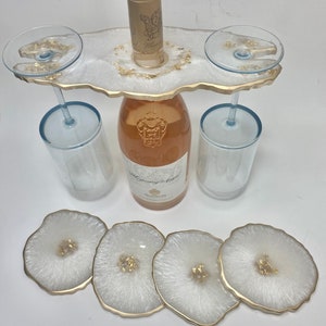 May include: White resin serving tray with gold accents, featuring two wine glass holders and a bottle holder. The tray is accompanied by three white coasters with gold accents.