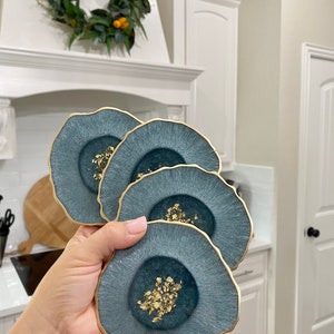 May include: Set of four blue and gold resin coasters with a wavy edge. Each coaster has a gold fleck design.