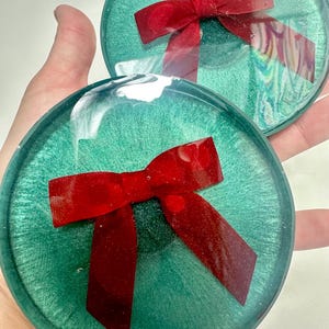 Moderne harsset met kerstdecor: groene onderzetters met traditionele fluwelen kerststrik, doorzichtige randen. Uniek gastvrouwcadeau
