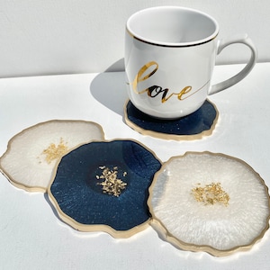 May include: Four coasters with gold flecks and a white mug with the word "Love" in gold lettering. Two coasters are white with gold flecks and two are dark blue with gold flecks.