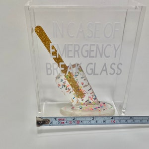 May include: A clear acrylic box containing a gold glitter-covered popsicle. The box has the text "IN CASE OF EMERGENCY BREAK GLASS" printed on the side.