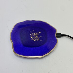 May include: A purple wireless charging pad with a gold rim and gold flecks embedded in the resin. The charging pad is connected to a black charging cable.