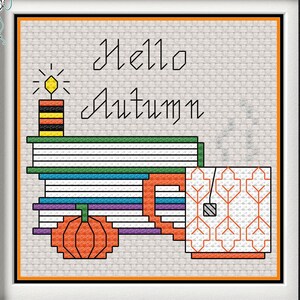 May include: Cross stitch pattern featuring a stack of books, a lit candle, a pumpkin, and a mug with a leaf pattern. The text "Hello Autumn" is stitched above the objects.