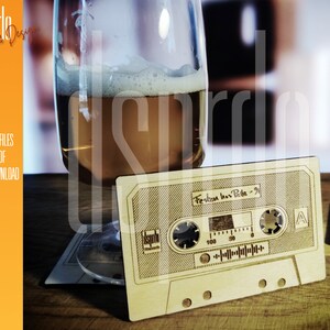 May include: A wooden cassette tape coaster with the text "Festen hos Pelle - 91" engraved on it. The coaster is sitting on a wooden surface next to a glass of beer.