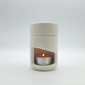 Puede incluir: Difusor de aceite de cerámica blanca con una pequeña vela de té en su interior. El difusor tiene un diseño recortado que permite que el calor de la vela derrita la cera.