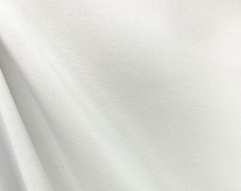May include: Close-up of a white fabric with visible texture and folds. The fabric appears to be a light, neutral color, possibly cotton or a similar material. The folds create shadows and depth, highlighting the texture.