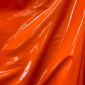 May include: A bright orange fabric with a glossy finish. The fabric is draped and folded, showing its texture and sheen.