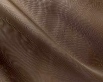 May include: A close-up of a brown sheer fabric with a subtle textured pattern. The fabric is draped and folded, creating soft, flowing lines.