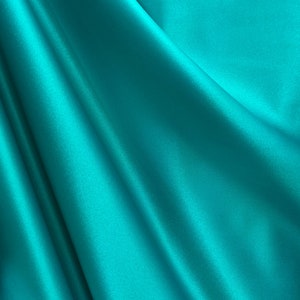 May include: A smooth, teal blue fabric with soft folds and wrinkles. The fabric has a silky sheen and a luxurious feel.