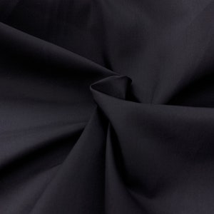 May include: Close-up of a dark navy blue fabric with soft folds and subtle shadows. The material appears smooth and opaque, with a slight sheen. The fabric is likely used for clothing or home decor.