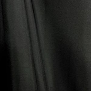 May include: Black fabric with a smooth, slightly textured surface. The fabric is draped and folded, creating soft, flowing lines.