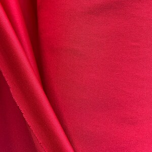 May include: A close-up of a vibrant red fabric with a smooth, textured surface. The fabric is folded in a way that creates a soft, flowing drape.