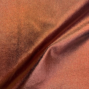 May include: Close-up of a shimmering fabric with a metallic sheen. The material has a rich, warm color, transitioning from copper to a deeper reddish-brown. The texture appears smooth with subtle folds.