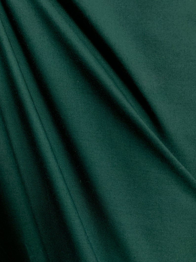 May include: A close-up of a dark green fabric with a smooth texture and subtle folds.