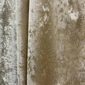 May include: Close-up of a beige fabric with a crocodile-embossed pattern. The fabric has a soft, velvety texture.