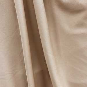 May include: A close-up of a smooth, beige fabric with a subtle sheen. The fabric is folded in a way that creates soft, flowing lines.