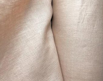 May include: Close-up of a beige linen fabric with a subtle texture. The fabric is folded, creating soft shadows and highlighting the natural weave. The neutral color suggests a versatile textile suitable for various applications.