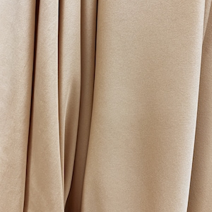 May include: Close-up of a smooth, beige fabric with a subtle texture. The fabric is folded in a way that creates soft, flowing lines.