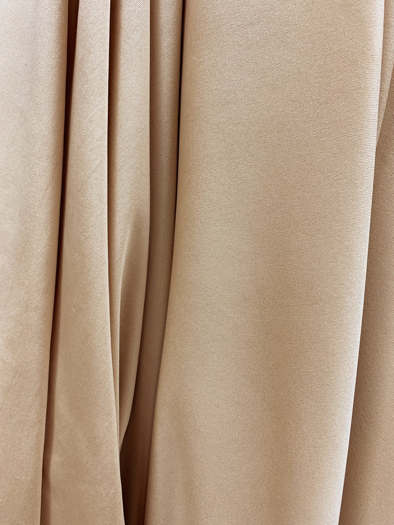May include: Close-up of a smooth, beige fabric with a subtle texture. The fabric is folded in a way that creates soft, flowing lines.