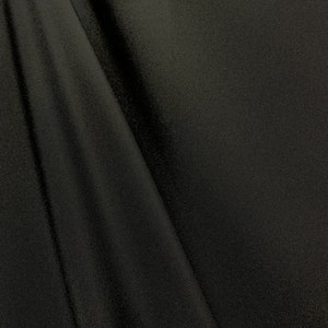 May include: Black fabric with a smooth, slightly textured surface. The fabric is folded and draped, creating soft folds and curves.
