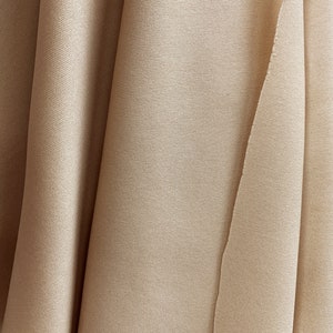 May include: A close-up of a beige fabric with a smooth texture. The fabric is folded in a way that creates a series of soft curves.