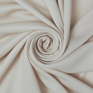 May include: Close-up of a cream-colored fabric, tightly swirled to create a spiral pattern. The fabric has a subtle texture and a soft, neutral tone, ideal for apparel or home decor.