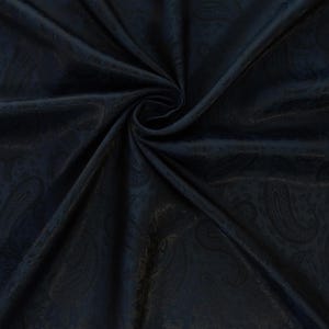 May include: Dark navy blue paisley fabric with a swirling pattern. The fabric has a subtle sheen, and the paisley design is visible throughout the material. The fabric is folded and draped, creating a sense of depth and texture. Ideal for apparel and home decor.