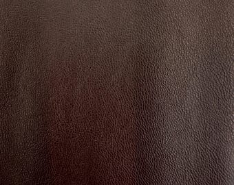 May include: Close-up of a dark brown leather texture. The leather has a pebbled surface and a subtle sheen.