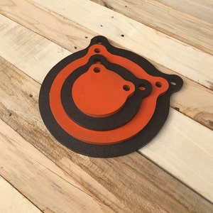 May include: Three round shooting targets, the largest is black with an orange ring, the middle is orange with a black ring, and the smallest is orange. All three targets have two holes at the top.