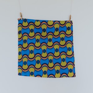May include: A blue and yellow fabric with a repeating pattern of circles and waves. The fabric is hanging from two clothespins.