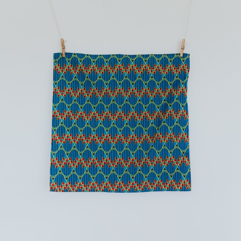 May include: A blue fabric with a repeating pattern of red, yellow, and green geometric shapes. The fabric is hanging from two clothespins.
