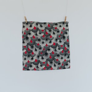 May include: A black and white patterned fabric with red teardrop shapes. The fabric is hanging from two clothespins.