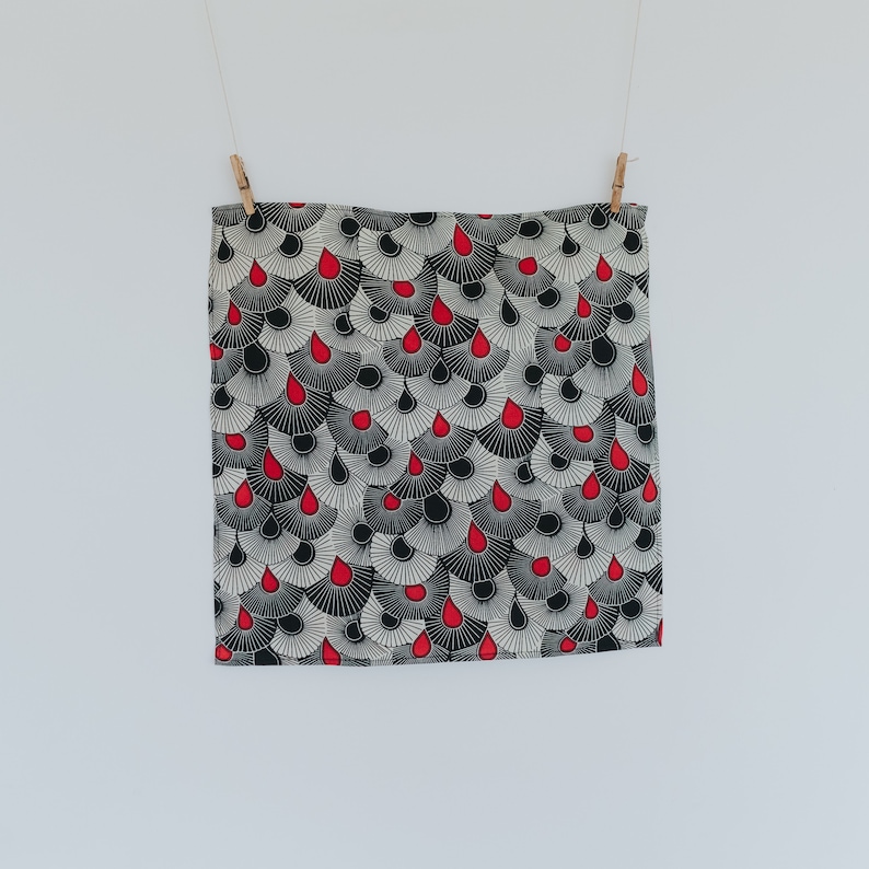 May include: A black and white patterned fabric with red teardrop shapes. The fabric is hanging from two clothespins.