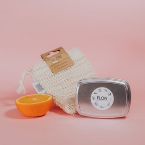 Pode incluir: Uma bolsa de malha branca com uma etiqueta marrom que diz "FLON". Um recipiente de metal prateado com um adesivo branco que diz "FLON". Uma meia laranja em uma superf&iacute;cie rosa.