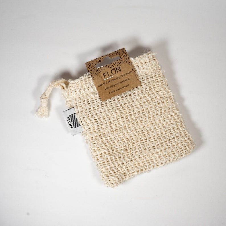 Pode incluir: Um saco de sab&atilde;o de sisal natural com fecho de cord&atilde;o. O saco &eacute; feito de um material tecido bege e est&aacute; etiquetado "FLON Saco de sab&atilde;o de sisal natural / Toalha de lavagem Limpeza e esfolia&ccedil;&atilde;o Um produto zero desperd&iacute;cio".
