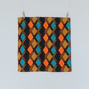 May include: A brown fabric with a geometric pattern of orange, yellow, blue, and green diamonds. The fabric is hanging from two clothespins.